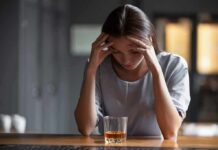 Addiction Cure? The Treatment Trap Woman with head in hands at a bar with a glass of whiskey