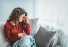 Woman sitting on couch holding pills and rubbing her forehead