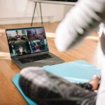 person on yoga mat watching a virtual workout class on a laptop