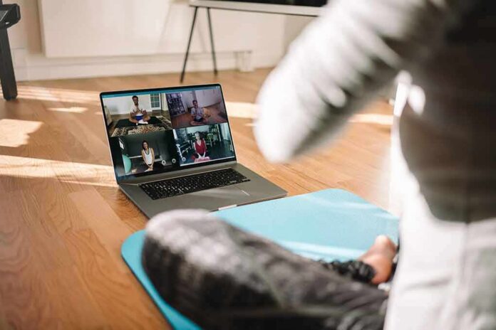 person on yoga mat watching a virtual workout class on a laptop