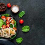 Grilled chicken salad with avocado, tomatoes, and spinach on a dark plate