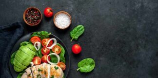 Grilled chicken salad with avocado, tomatoes, and spinach on a dark plate