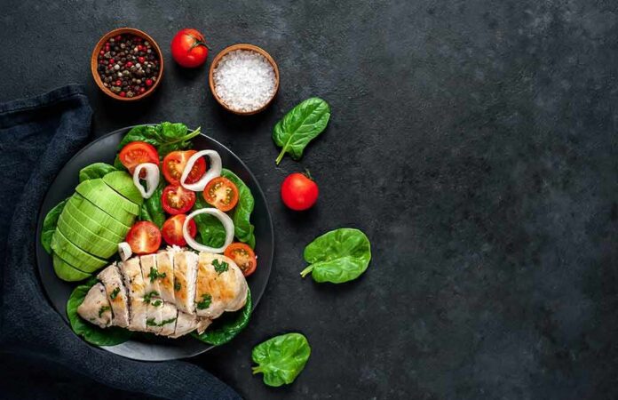 Grilled chicken salad with avocado, tomatoes, and spinach on a dark plate