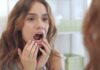 young woman checking inside her mouth in bathroom mirror