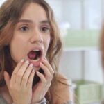 What if you didn’t brush your teeth for a year? young woman checking inside her mouth in bathroom mirror
