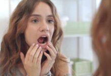young woman checking inside her mouth in bathroom mirror