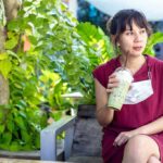 Woman in red dress drinking iced matcha in a garden