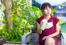 Woman in red dress drinking iced matcha in a garden