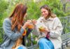 Two women sitting on a park bench eating takeout bowls