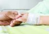 A person holding the hand of a patient with an IV in a hospital bed