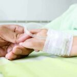 A person holding the hand of a patient with an IV in a hospital bed
