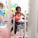 Woman lunging on sled in gym next to man using cable machine