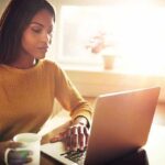 Woman working on a laptop with a mug in hand
