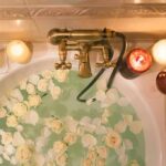 Bathtub filled with water and white roses under candles
