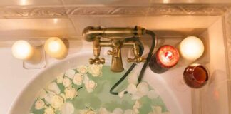 Bathtub filled with water and white roses under candles