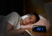 Person in bed looking at a digital alarm clock reading 2:21