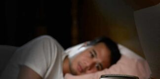 Person in bed looking at a digital alarm clock reading 2:21